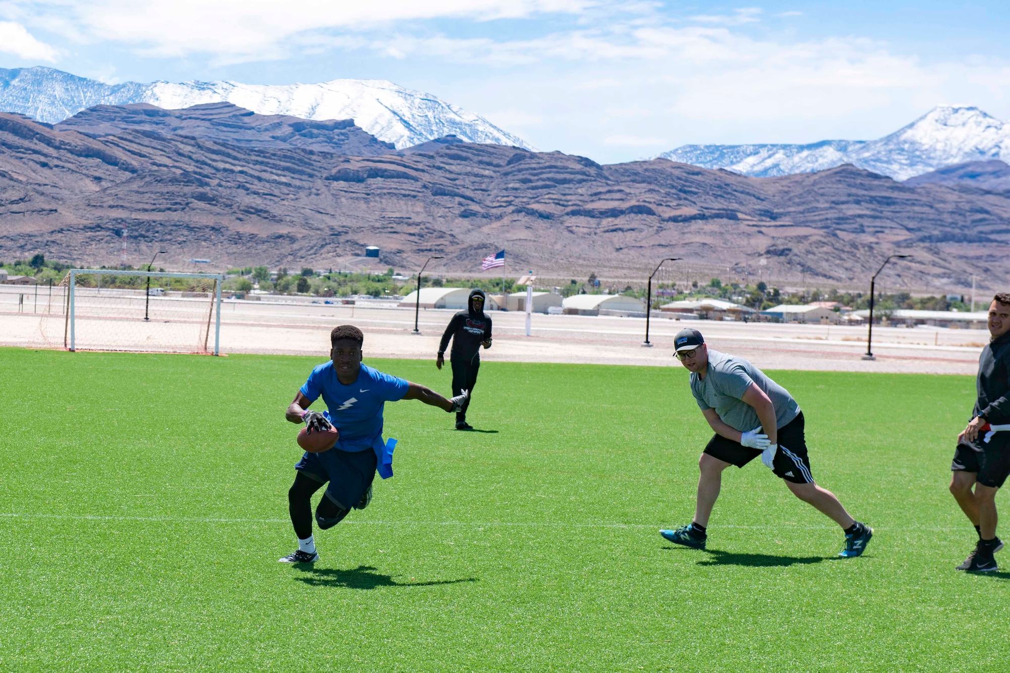 An airman sprints with a football on a turf field during a flag football game.