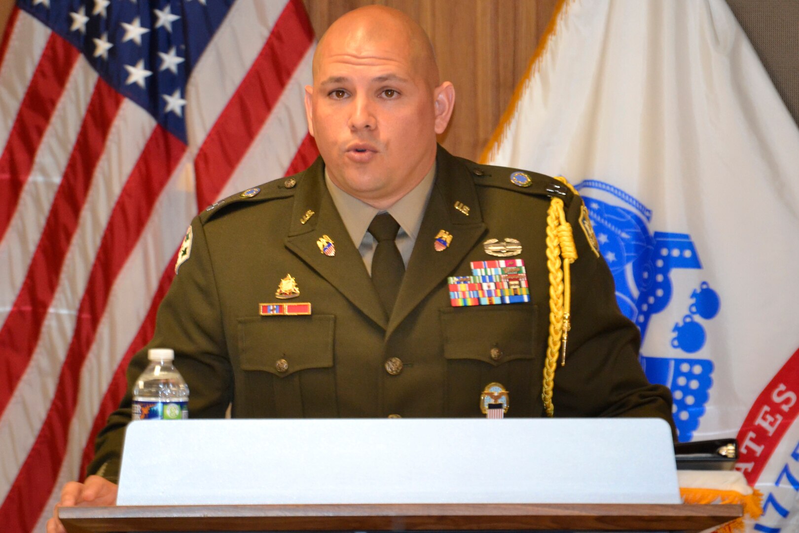 A man in Army service dress speaks from a podium