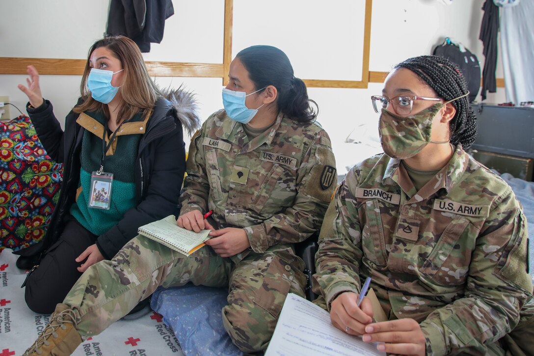 An Afghan interpreter, left, speaks to Afghan guests while U.S. Army Spc. Sandra Lara, center, assigned to 372nd Engineer Company, Transportation Company, Pewaukee, Wisconsin, and Pfc. Keyara Branch, right, assigned to 652nd Multi-Role Bridge Company, Ellsworth, Wisconsin, listen during Female Engagement Team visits at Fort McCoy, Wisconsin, Dec. 23, 2021. The FET is an all women team of interpreters, Soldiers and a gender advisor. The Department of Defense, through U.S. Northern Command, and in support of the Department of Homeland Security, is providing transportation, temporary housing, medical screening, and general support for at least 50,000 Afghan evacuees at suitable facilities, in permanent or temporary structures, as quickly as possible. This initiative provides Afghan personnel essential support at secure locations outside Afghanistan. (U.S. Army photo by Yesenia Barajas, 7th Mobile Public Affairs Detachment)