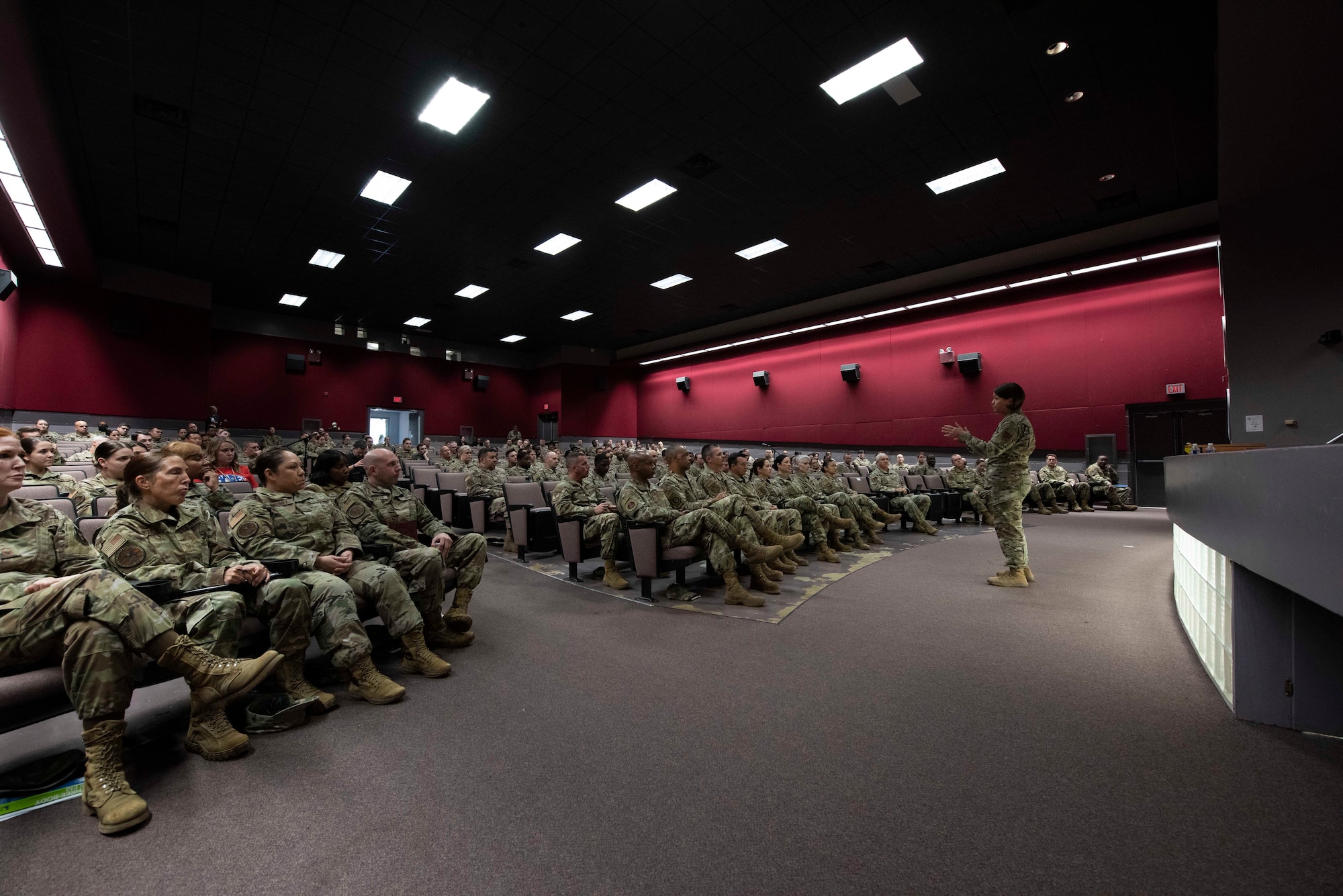 Large group of Airmen sitting in an auditorium listening as one Airmen standing at front speaking.