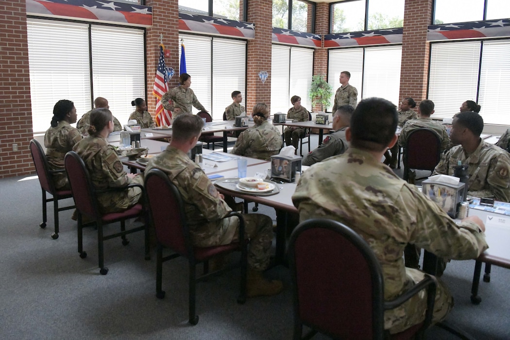 Airmen sitting around tables eating food while talking.