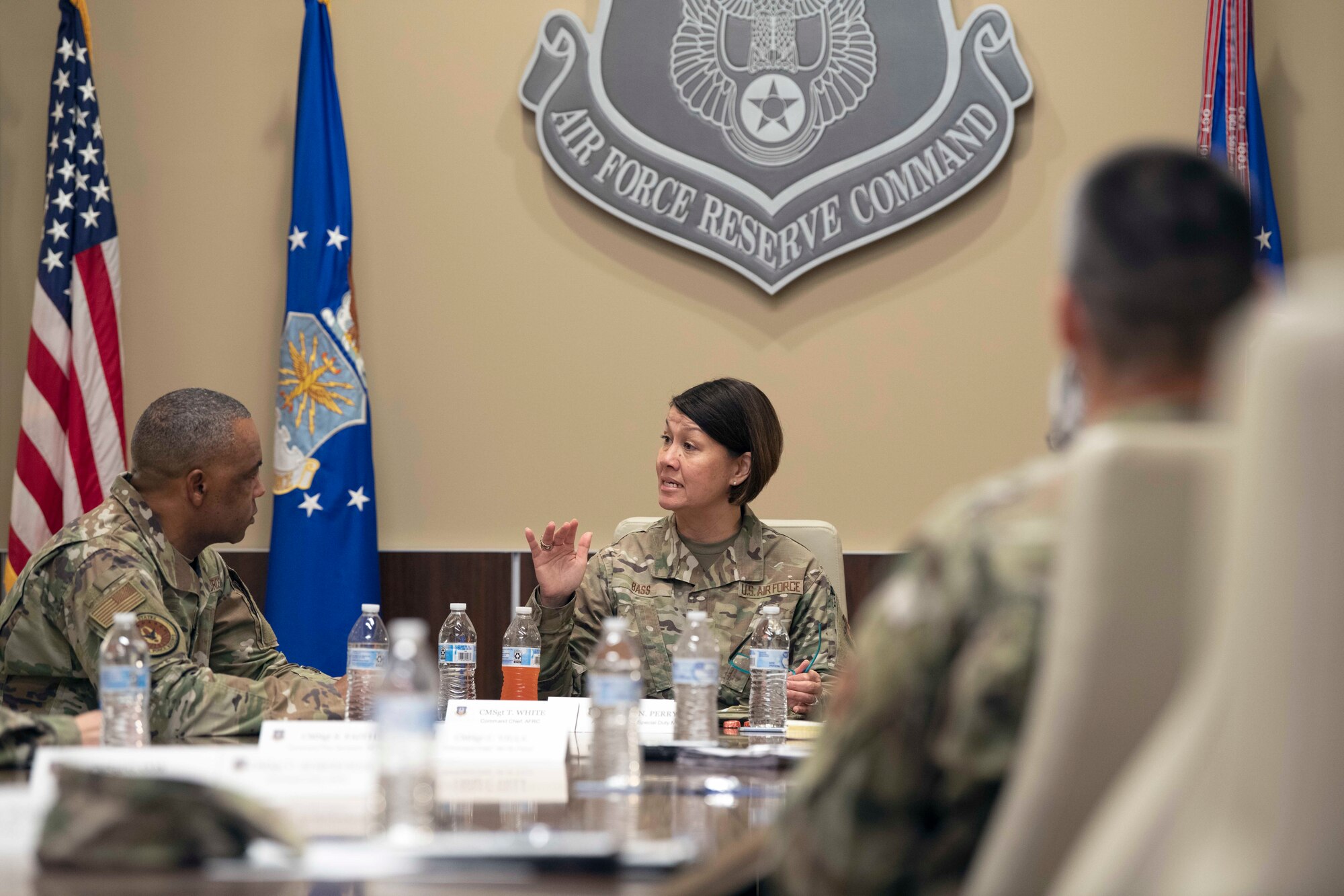 Airmen sitting at table in conference room speaking to one another.