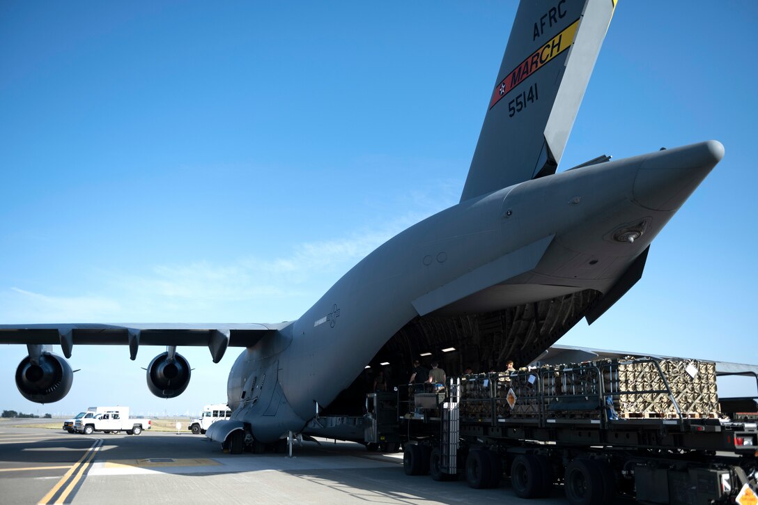 A vehicle carrying supplies is parked in front of an airplane’s open cargo hold with people inside.