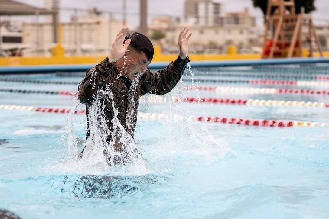 A Marine raises his arms while standing in a pool.