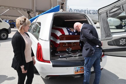 Two peolple pay respects to a flag draped coffin placed in a hearst.
