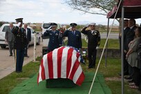 Uniformed veterans and an honor guard soldier salute the American flag draped casket of a deceased soldier.