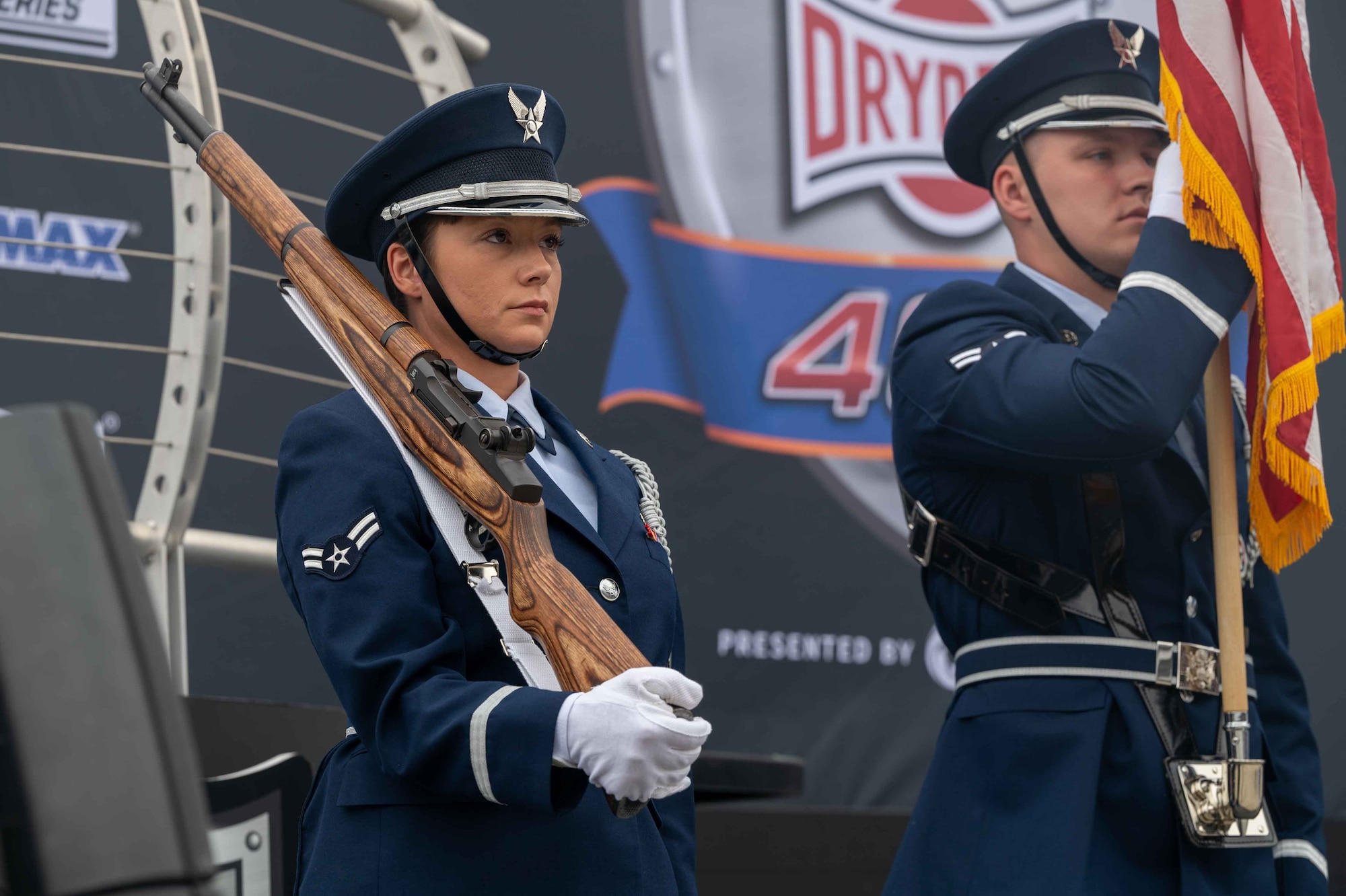 From the left, Airman 1st Class Laci Churchill, and Airman 1st Class Noah Preisch, both Dover Air Force Base Honor Guard members, present the colors before the Drydene 400 at Dover Motor Speedway in Dover, Delaware, May 1, 2022. Honor Guard members presented the colors during pre-race events throughout the 2022 NASCAR weekend. (U.S. Air Force photo by Senior Airman Faith Schaefer)