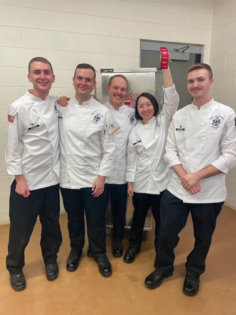 The Coast Guard's student team members during the culinary competition, the 46th Joint Culinary Training Exercis, March 10, 2022. The team won silver in the Student Chef of the Year category and Petty Officer 3rd Class Predmore won Student Chef of the Year. Pictured from left to right: Petty Officer 3rd Class Declan Dormburg, Petty Officer 3rd Class Spencer Hooker, Petty Officer 3rd Class Micah Hetrick, Petty Officer 3rd Class Joanni Govier and Petty Officer 3rd Class Thomas Predmore. (USCG photo)