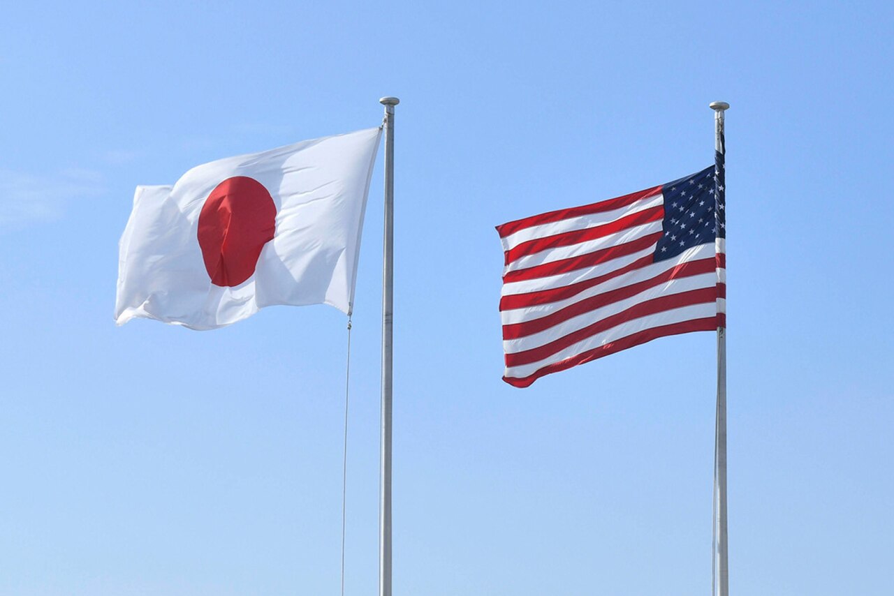 American and Japanese flag fly side-by-side against blue sky.
