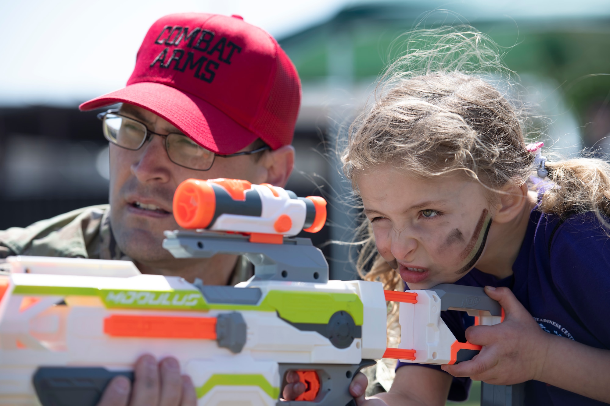 Senior Airman Chad Tavenner, 374th Security Forces Squadron combat arms instructor, left, assists, Kaleia Shealy, Operation Kids Understanding Deployment Operations, with a toy rifle during Operation K.U.D.O.S. at Yokota Air Base, Japan, April 30, 2022. Operations K.U.D.O.S. consisted of toy weapon training, a C-130J Super Hercules tour and a mock medical checkup to simulate a deployed environment. (U.S. Air Force photo by Tech. Sgt. Joshua Edwards)