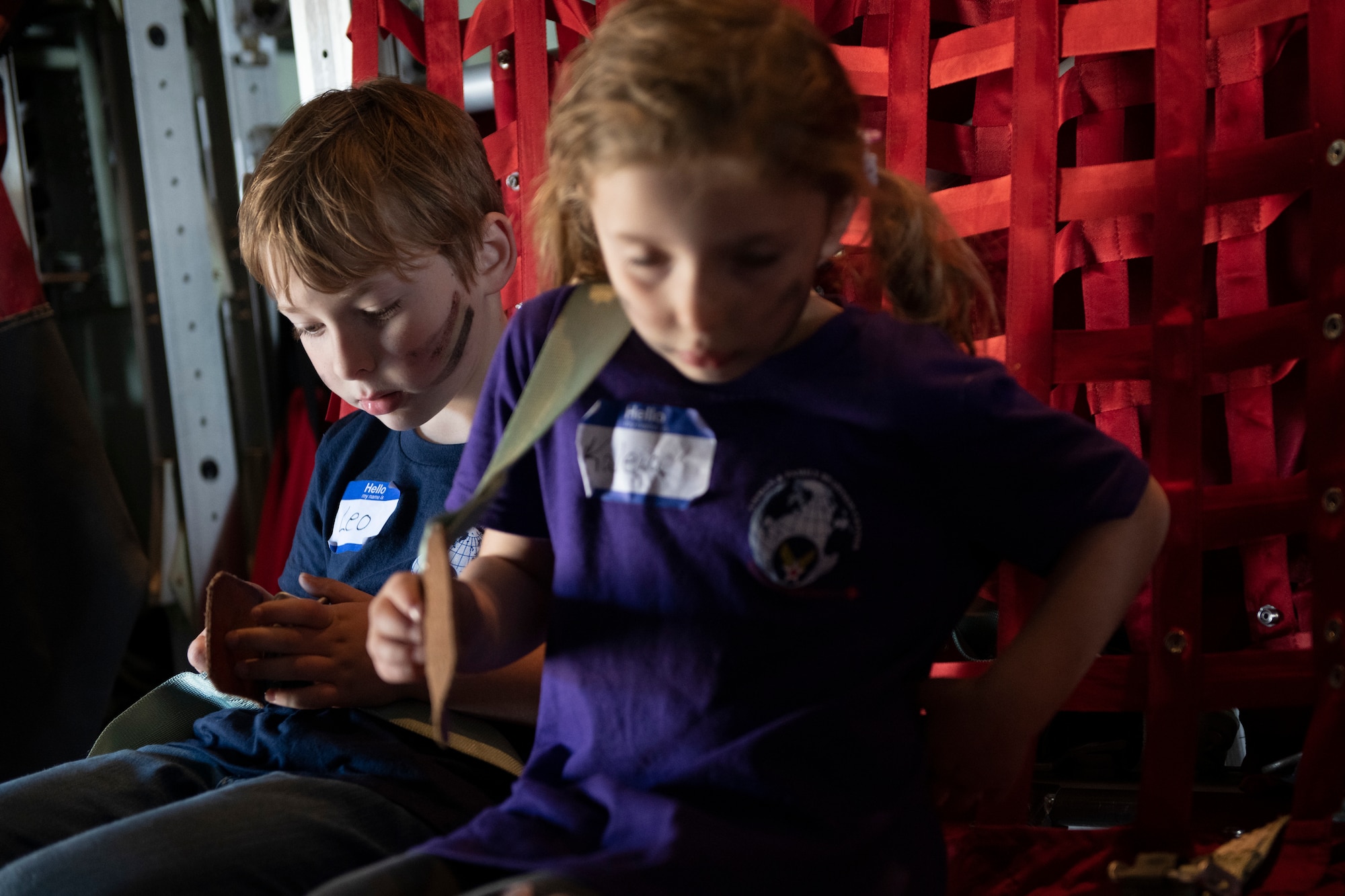 Leo, left and Kaleia Shealy, Operation Kids Understanding Deployment Operations participants, try to buckle into a C-130J Super Hercules seat during Operation K.U.D.O.S. at Yokota Air Base, Japan, April 30, 2022. Operations K.U.D.O.S. consisted of toy weapon training, a C-130J Super Hercules tour and a mock medical checkup to simulate a deployed environment. (U.S. Air Force photo by Tech. Sgt. Joshua Edwards)
