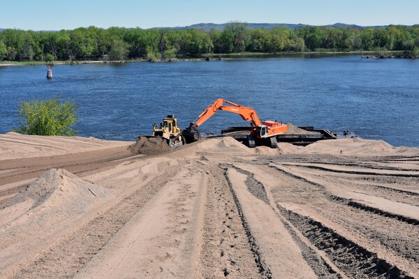 construction equipment moves sand near water.