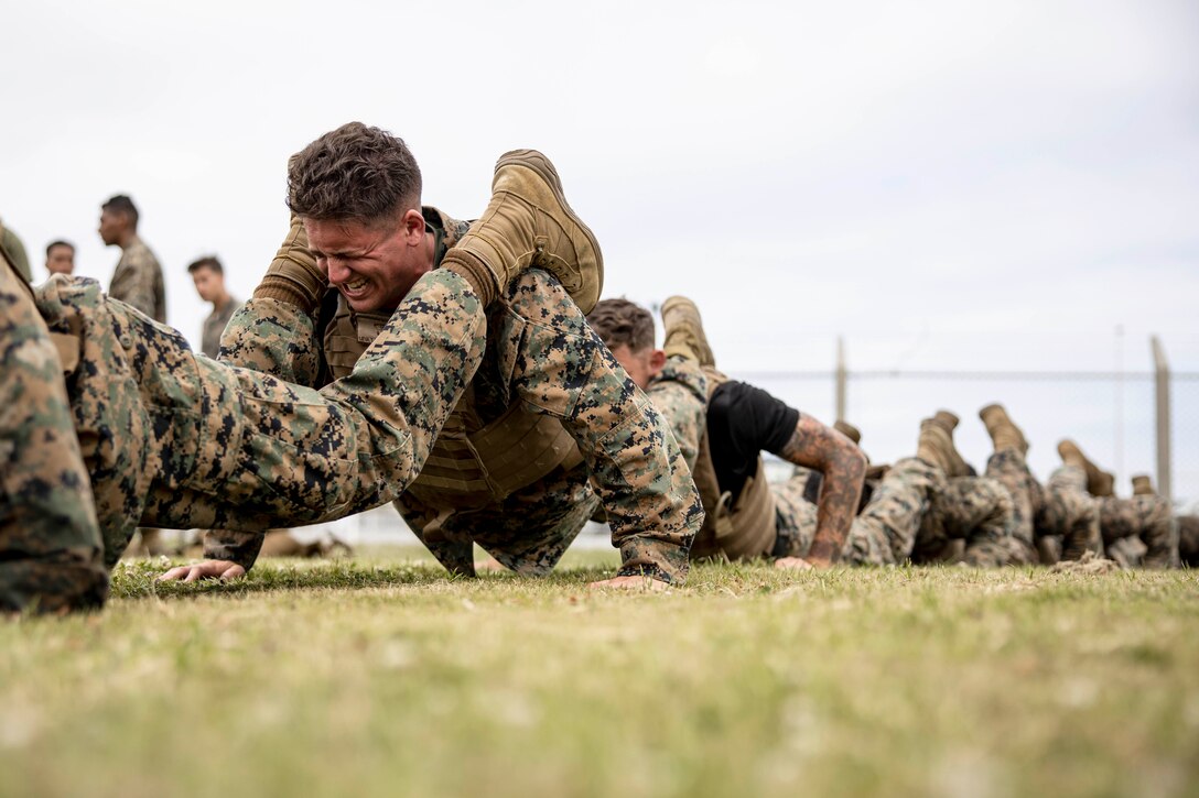 A row of Marines connect legs to shoulders while doing pushups.