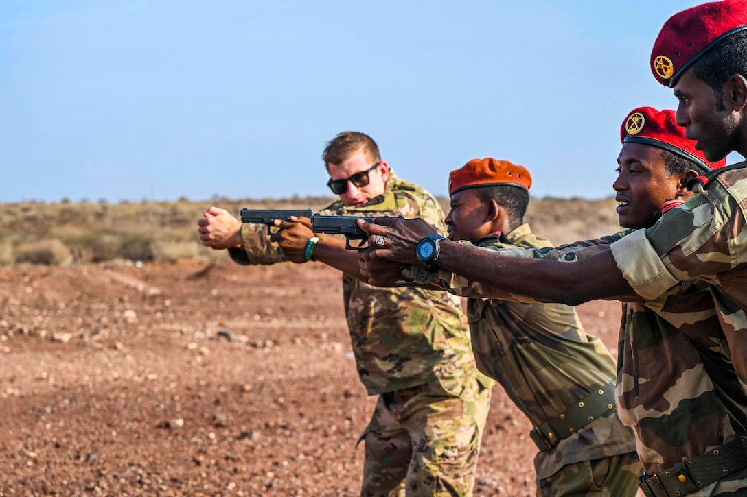 A soldier simulates holding a firearm next to troops holding out weapons.