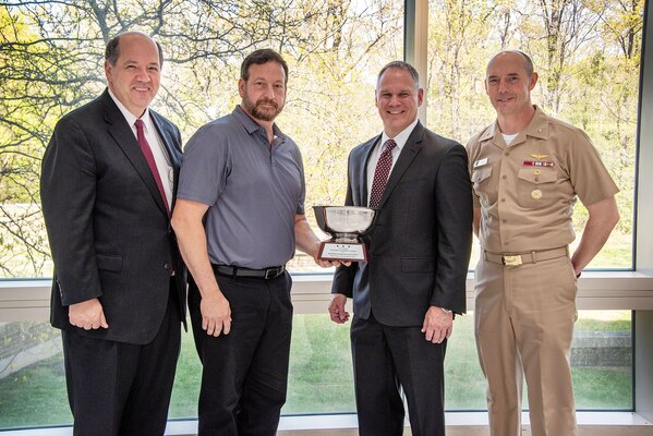 220420-N-HL559-0120 PATUXENT RIVER, Md. (April 28, 2022) Deputy Commander, Naval Air Systems Command (NAVAIR) Tom Rudowsky (left), presents the Annual Commander’s Award for Best Performing Fleet Readiness Center Production Line to Rodney Boone (holding trophy) from Fleet Readiness Center Southeast’s Vertical Lift team, along with top leadership from Commander Fleet Readiness Centers (right/right) Mr. Roy Harris and RDML Joe Hornbuckle during an awards ceremony at NAVAIR headquarters (U.S. Navy Photo by Peter Fitzpatrick).