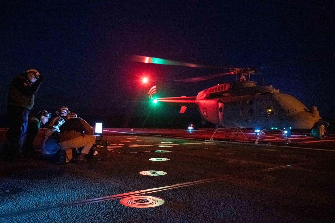 A lit helicopter sits on a ship at night.