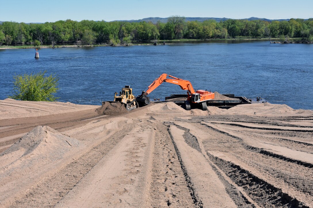 construction equipment moves sand near water.