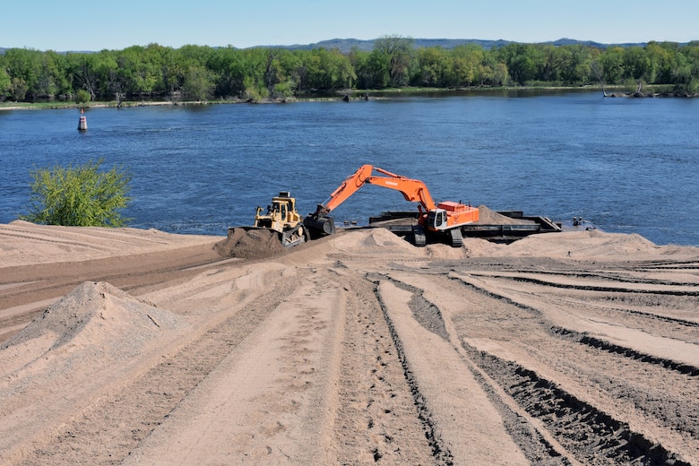 construction equipment moves sand near water.