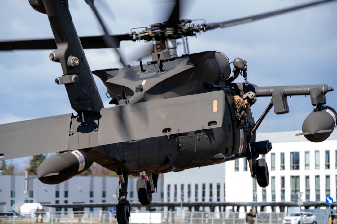 A Black Hawk helicopter takes off while a soldier looks out of the window.
