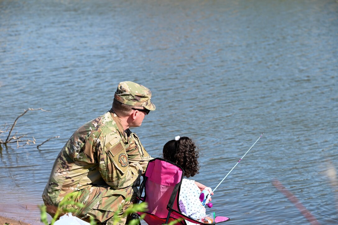 U.S. Air Force Master Sgt. Brett Devor, 97th Communications Squadron flight chief, hands a fishing pole to his daughter, Madison, during the second annual fishing derby, at Altus Air Force Base, Oklahoma, April 29, 2022. More than 80 Airmen and their family members attended the derby to catch catfish and celebrate Earth Day. (U.S. Air Force photo by Senior Airman Kayla Christenson)