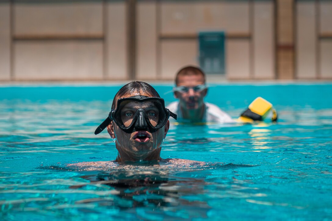 Two Marines in water goggles swim in a pool.