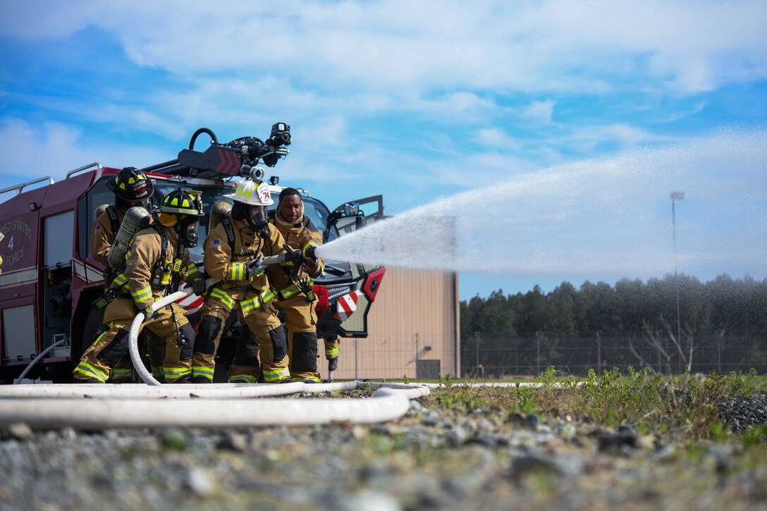 Several 316th Civil Engineer Squadron firefighters point a fire hose toward a simulated aircraft fire during an interagency fire-fight training at Joint Base Andrews, Md., May 2, 2022.