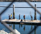 Sailors clean a dock in honor of Earth Day at Naval Station Everett in Everett, Washington April 22, 2022. The Navy is committed to strong environmental stewardship and is a U.S. government leader in sustainable energy programs. (U.S. Navy photo by Mass Communication Specialist 2nd Class Ethan Soto)