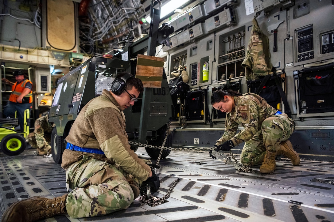 Two airmen secure cargo with chains in the cargo hold of an aircraft.
