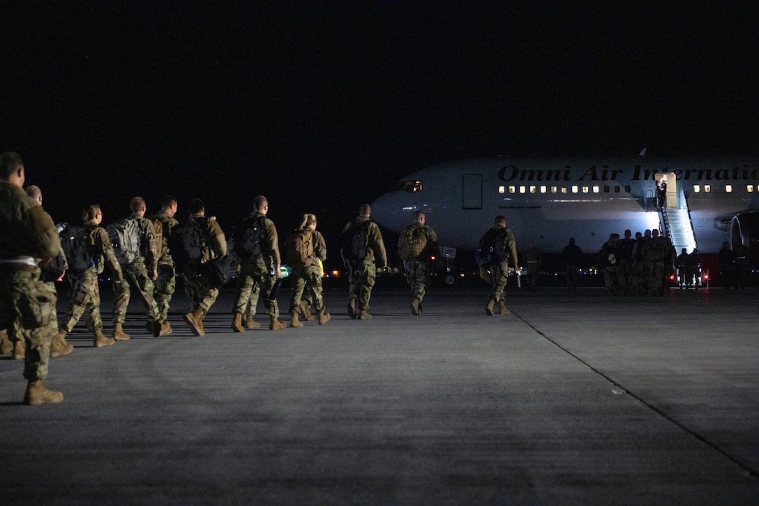 A line of airmen board a plane at night.