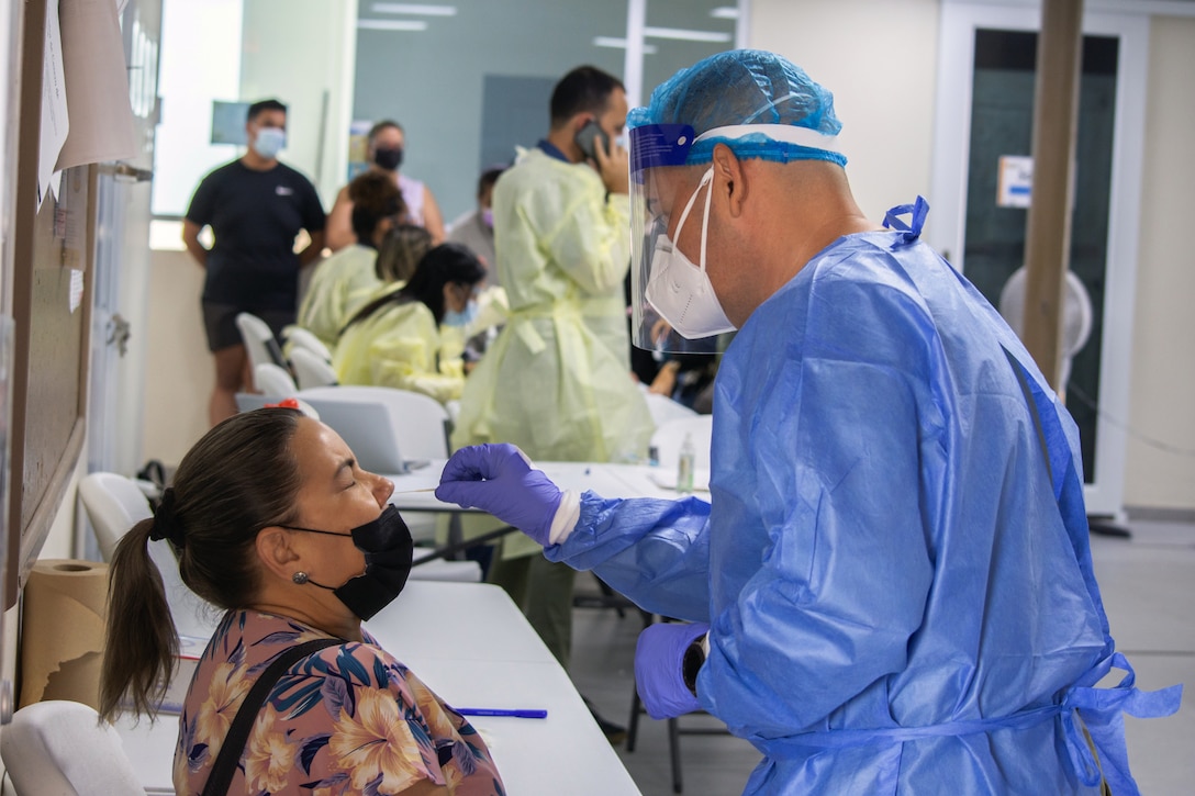 A man wearing medical personal protective equipment swabs a woman’s nasal cavity.