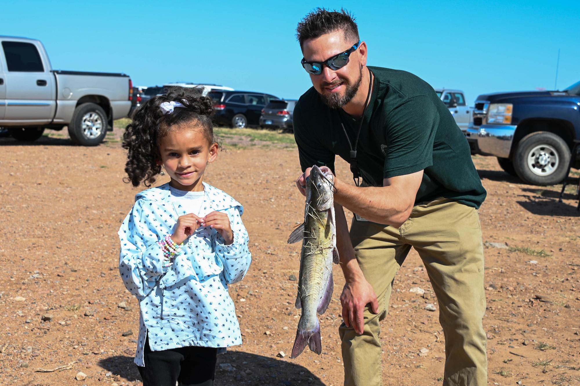 Mark Painter, 97th Civil Engineer Squadron environmental program manager, poses with a fishing derby attendee, Madison, and her recently-caught fish at Altus Air Force Base, Oklahoma, April 29, 2022. Fish were caught by anglers of all ages, lots of whom were children of active-duty service members. (U.S. Air Force photo by Senior Airman Kayla Christenson)