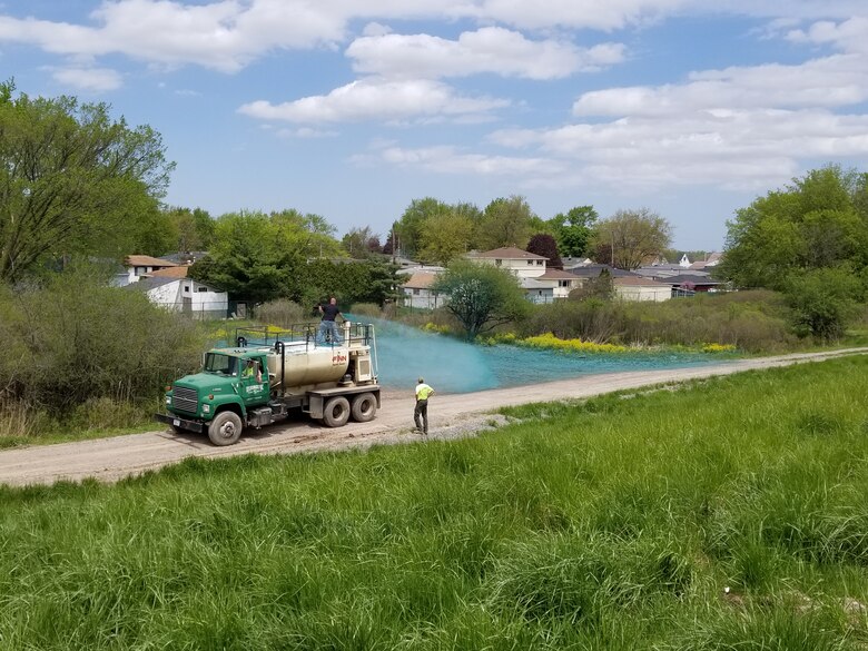 Green truck and two men spray seed on a green field.