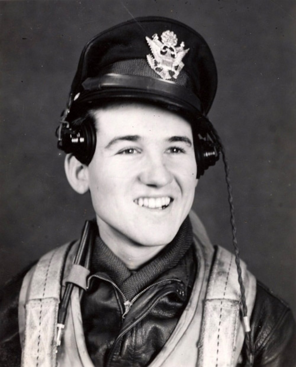 A young man wearing a cap, uniform and askew headphones smiles broadly as he poses for a black-and-white photo.