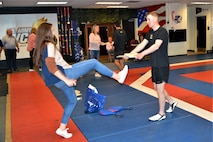 woman kicks a board to break it at a taekwondo demonstration that man is holding.