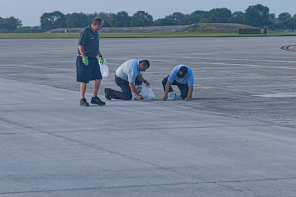 Three civilians pick up debris from runway area.