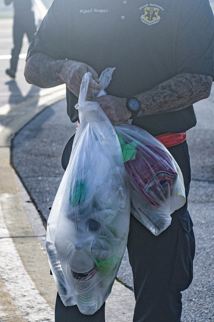 AF Civilian holding a clear trash bag with many items collected from a FOD walk.