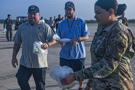 Airmen and AF Civilians walk towards collection point to drop items collected during a FOD walk.