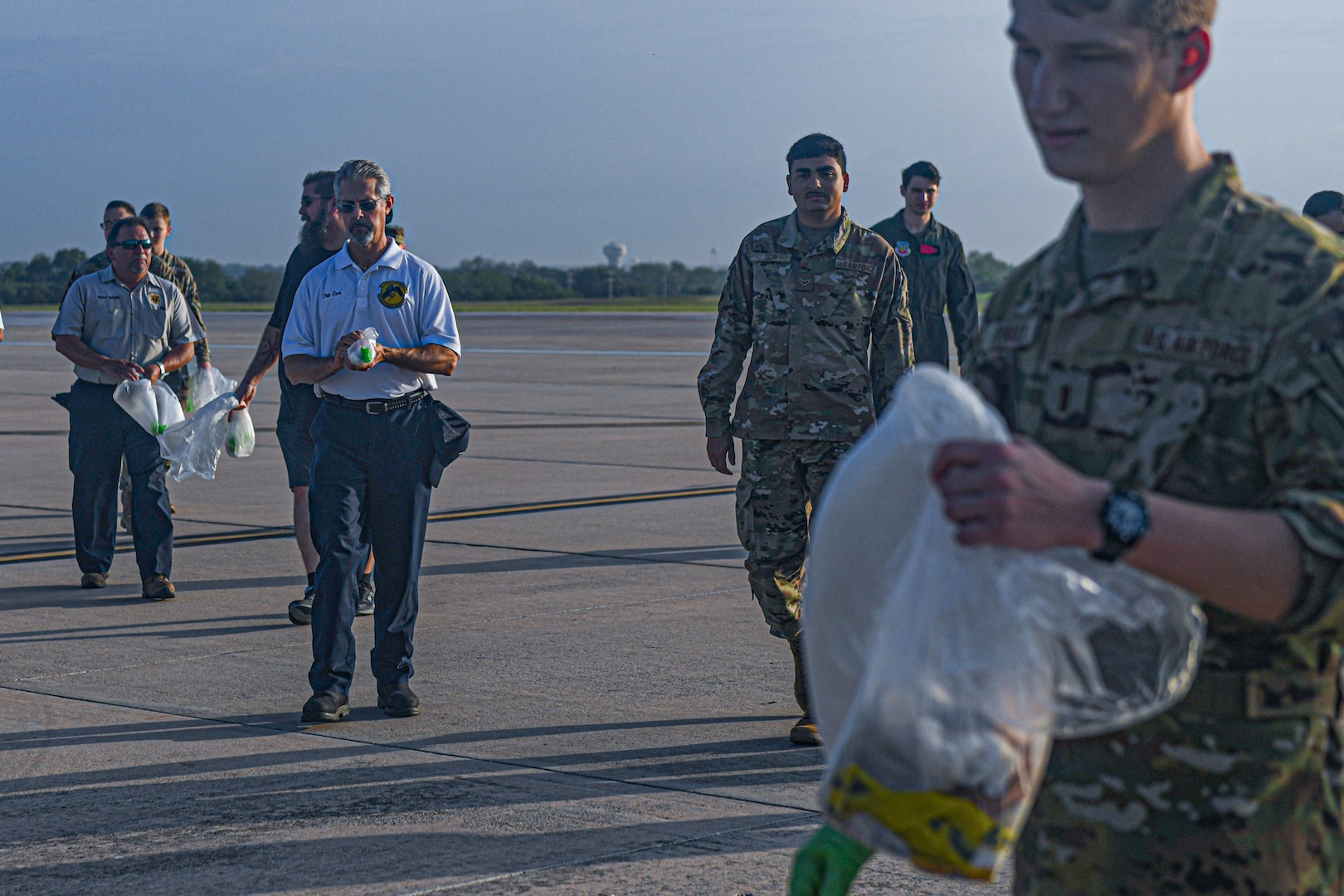 Airmen and AF civilians walk towards collection point to drop off FOD they collected from the walk on the flightline.