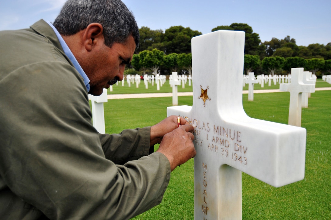 A man cleans golden lettering on a cross-shaped grave in a cemetery.