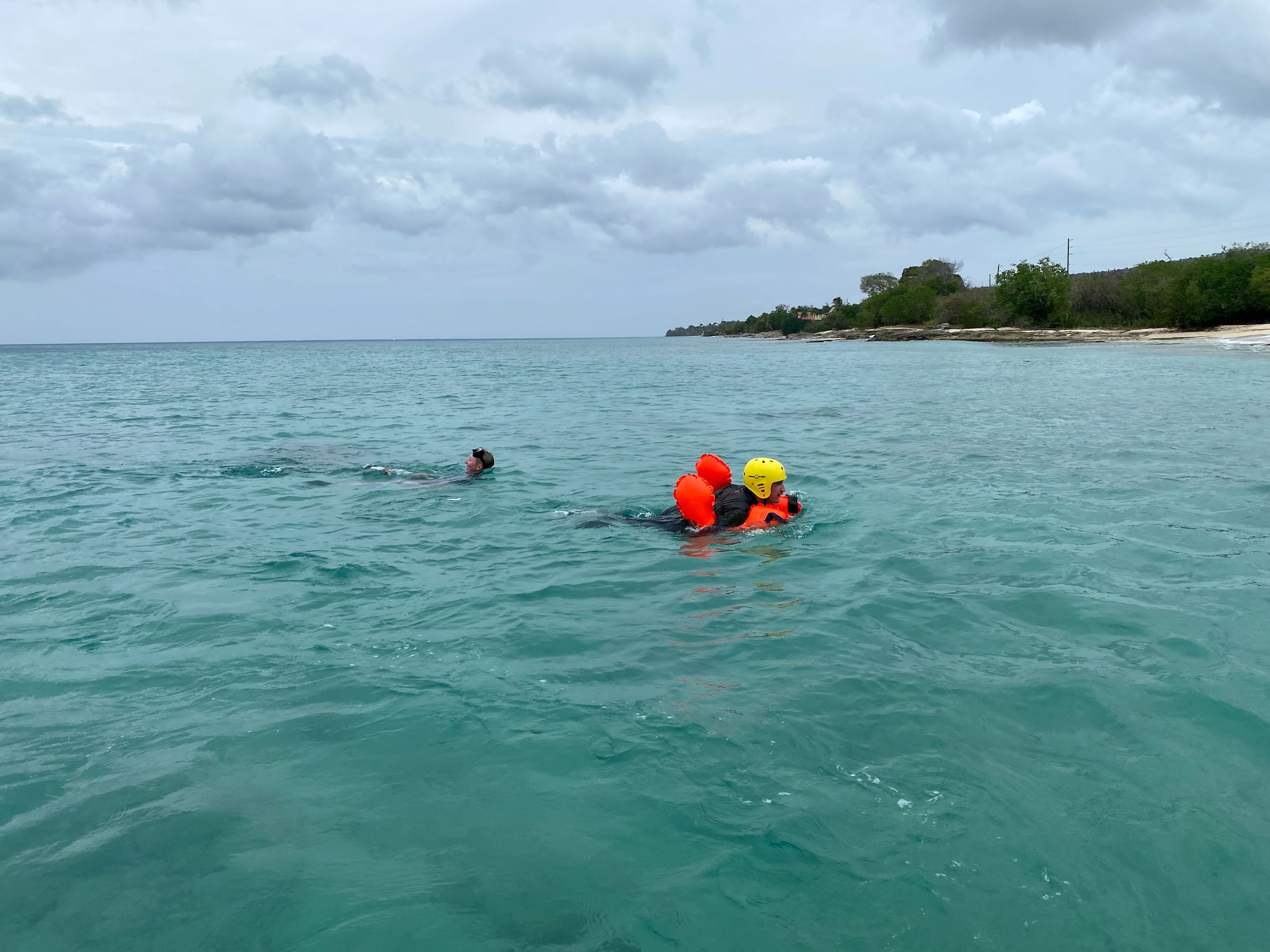 Two men swim in water. Beach and mountains in background