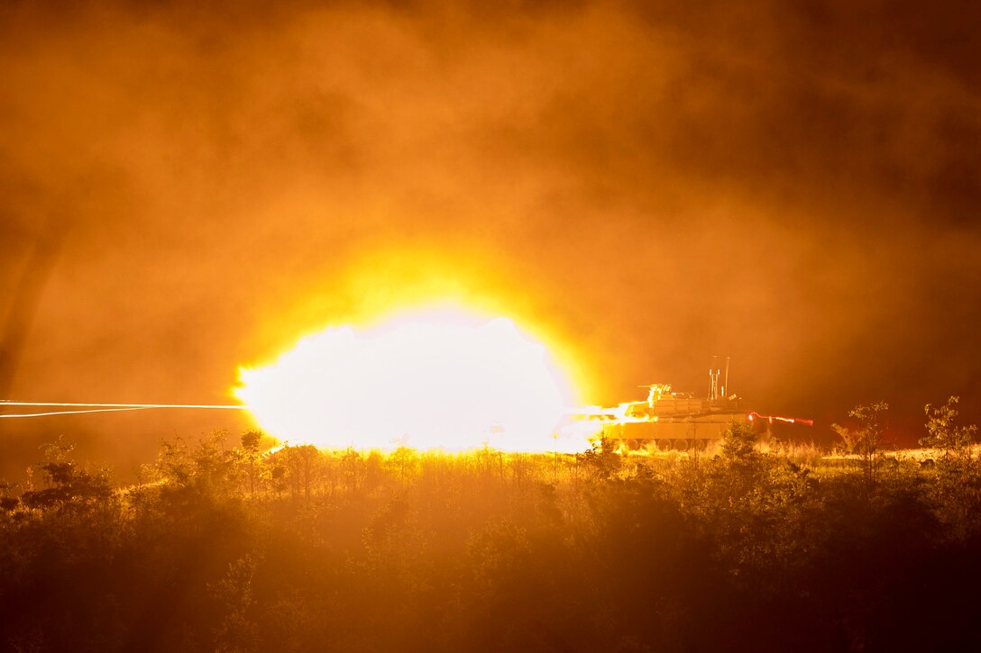 A tank fires at night in a field.