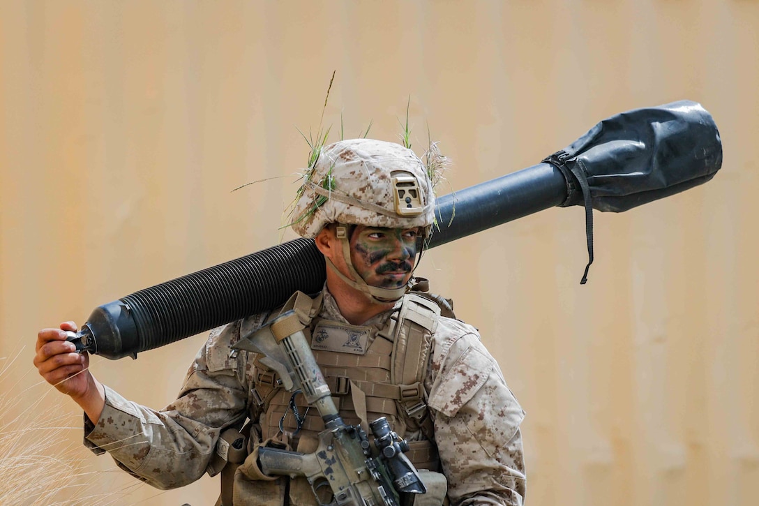 A Marine carries a large weapon on his shoulder.