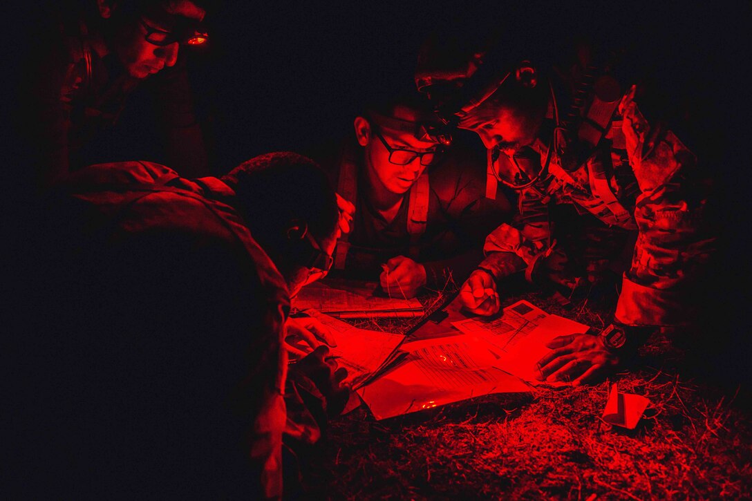 Service members look at a map under a red light at night.