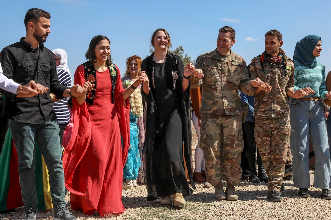 Soldiers and civilians standing in a row outside hold hands.