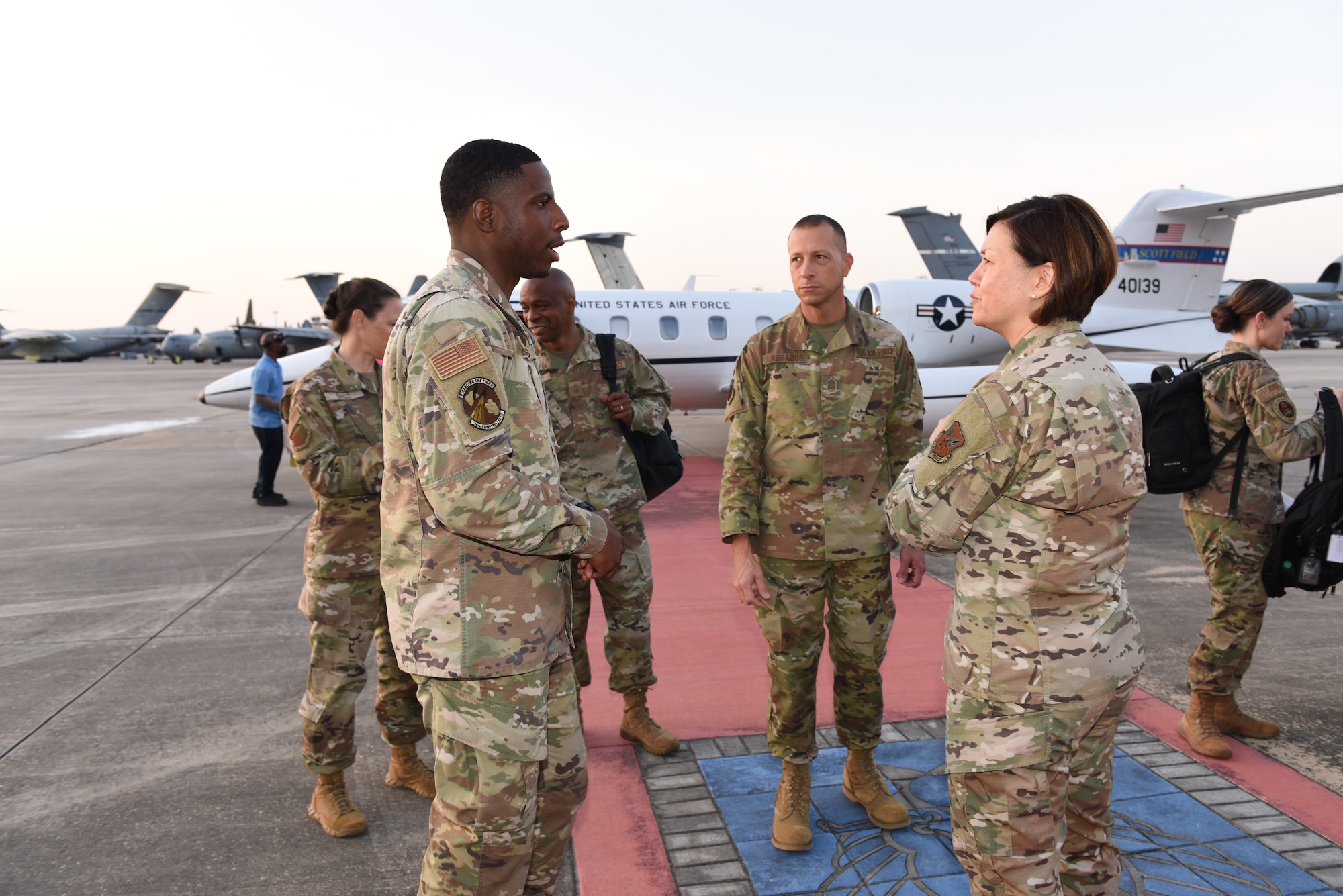 Photo shows group of people standing on flight line in front of plane.