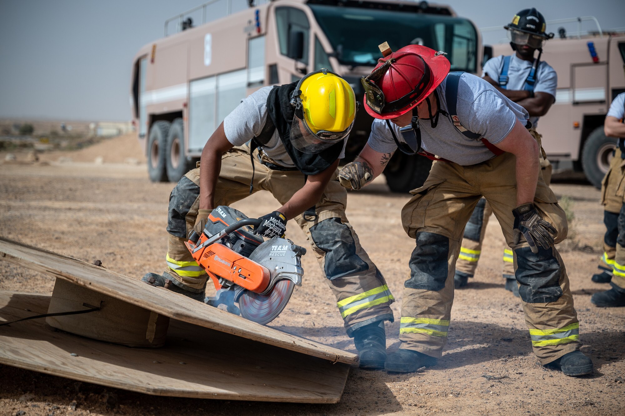Airman First Class Melvin Turner, 332d Expeditionary Civil Engineer Squadron firefighter, receives on-the-job training from Tech. Sgt. Joseph Donahue, 332d ECES firefighter, while operating a rotary saw during live-fire flashover training at an undisclosed location in Southwest Asia, April 30, 2022. (U.S. Air Force photo by Master Sgt. Christopher Parr)