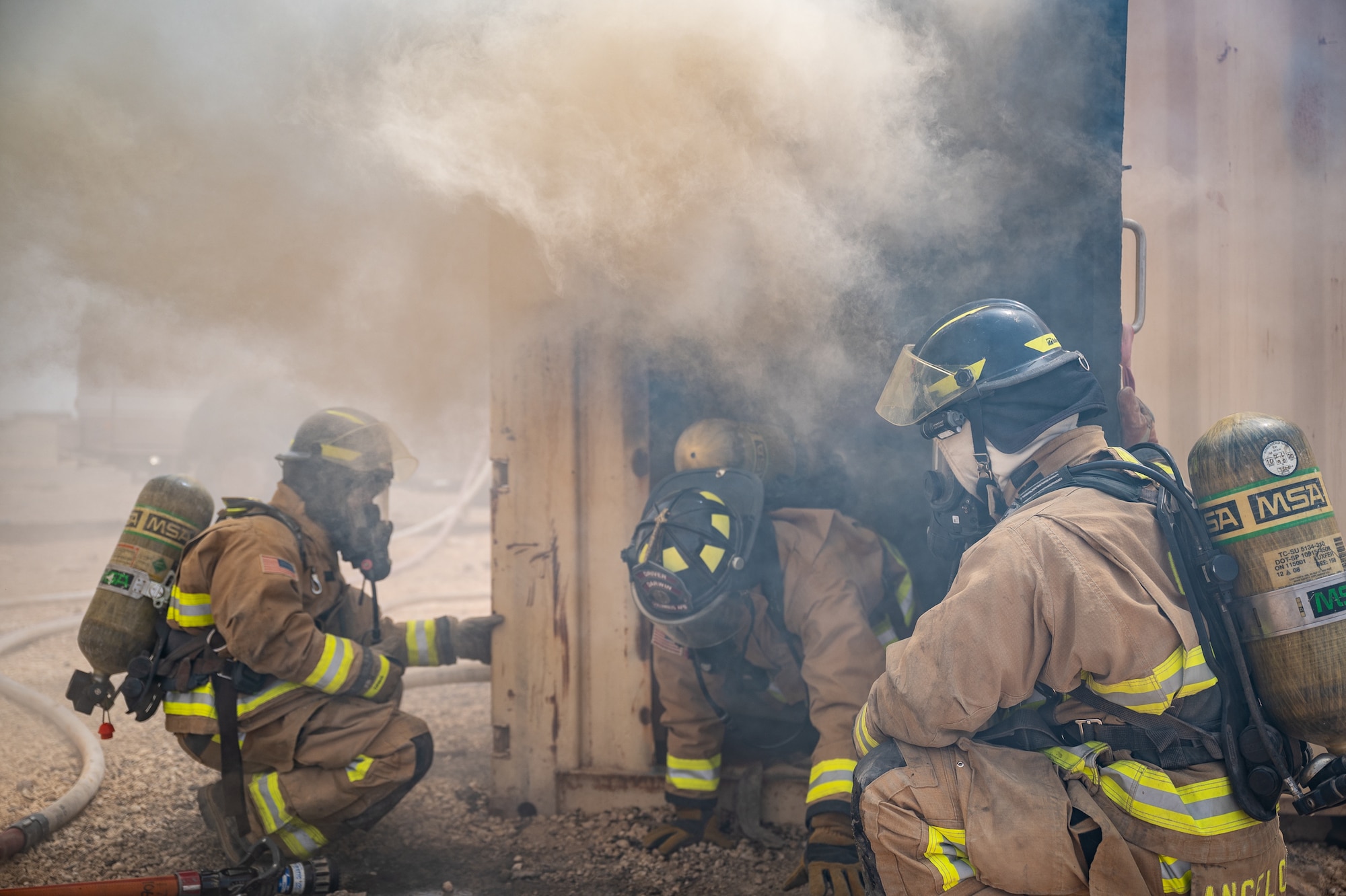 Two 332d Expeditionary Civil Engineer Squadron firefighters ensure students egress properly from the flashover trainer during live-fire flashover training at an undisclosed location in Southwest Asia, April 30, 2022. In addition to ensuring proper egress procedures are followed, the two firefighters also monitor the flashover trainer for safety concerns such as fire flare-ups. (U.S. Air Force photo by Master Sgt. Christopher Parr)