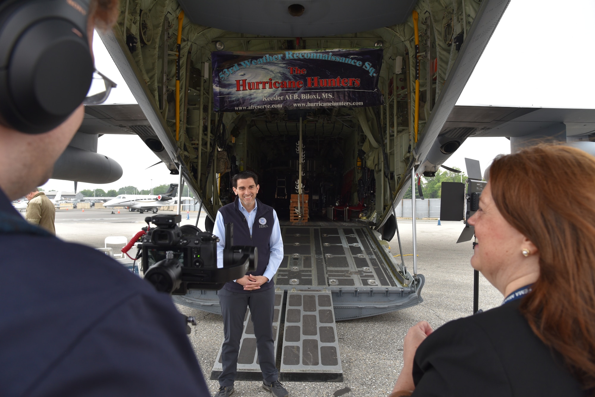 FEMA members video another FEMA member speaking about preparedness behind an Air Force Reserve WC-130J Super Hercules.