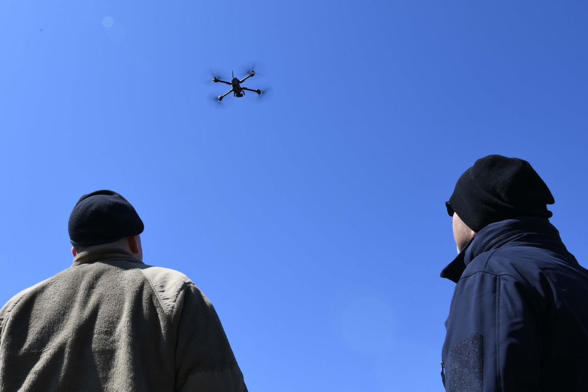 Senior Airman Michael Engleman, 319th Security Forces Squadron installation entry controller, and Steven Passement, Skydio technical training instructor watch as the drone prepares to land during an unmanned aircraft system flight training course at the University of North Dakota, Grand Forks, North Dakota, April 27, 2022. The drone can scan skies and fly low in obstacle dense, hard to reach areas such as cliffs, river banks, ravines and ditches. (U.S. Air Force photo by Senior Airman Ashley Richards)