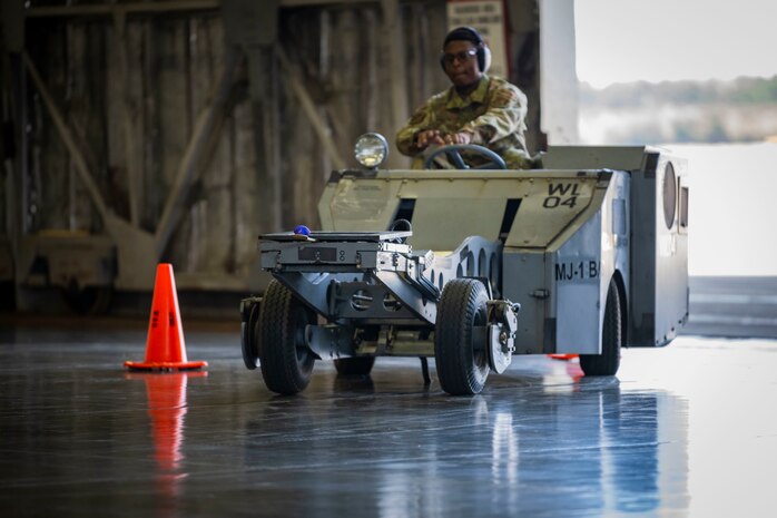 Military member in uniform drives a lift truck between cones.